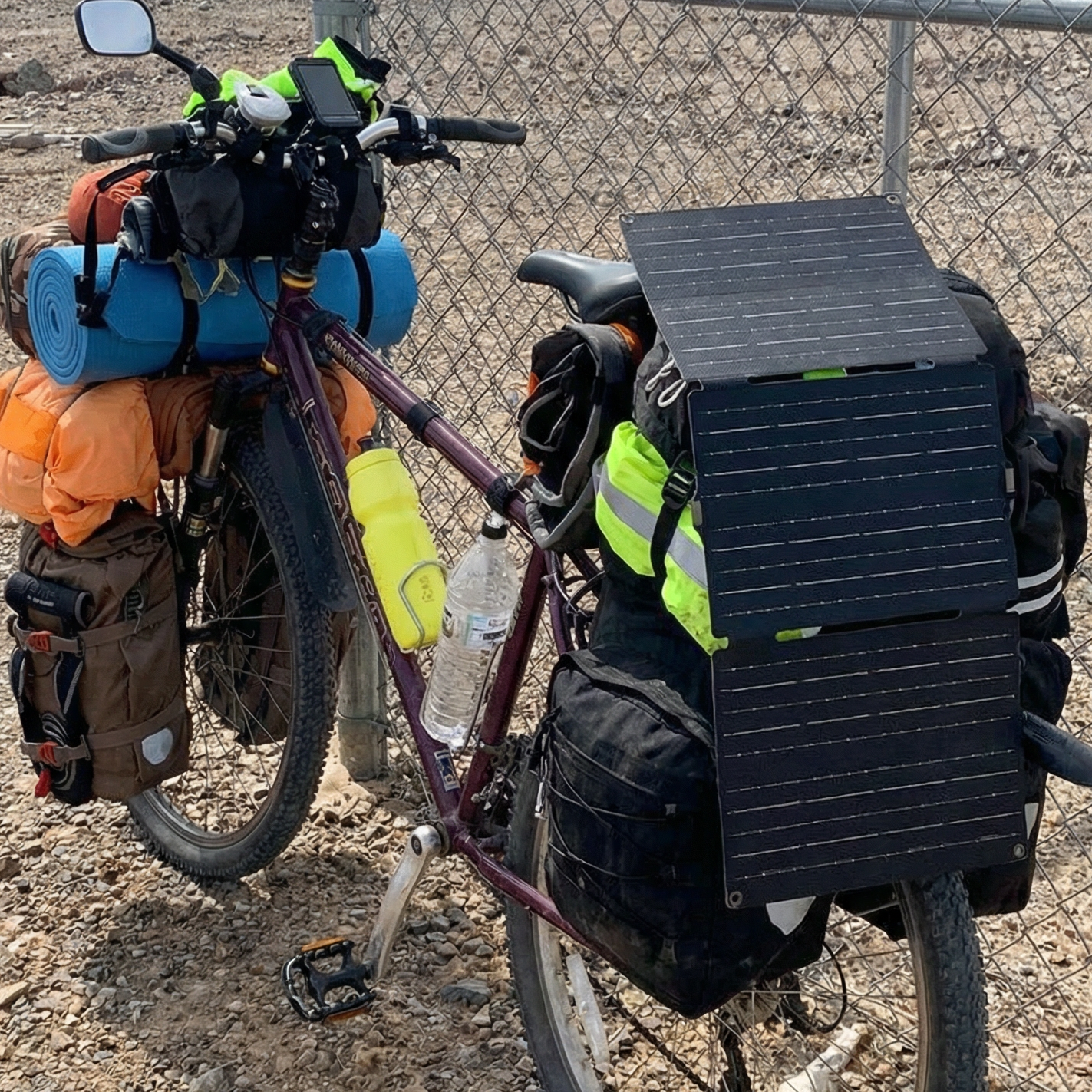 Bicycle loaded with camping gear and a solar panel on a dirt road.