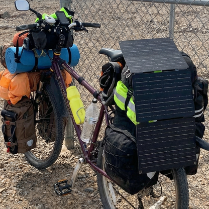 Bicycle loaded with camping gear and a solar panel on a dirt road.