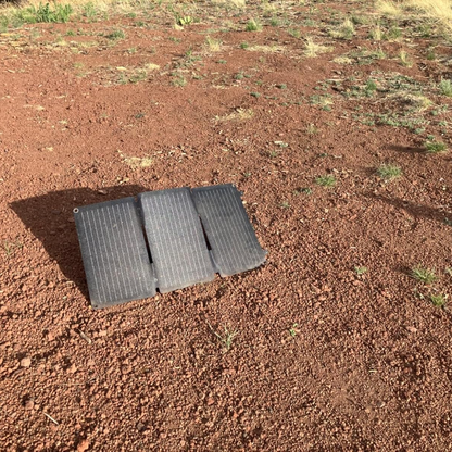 Two black solar panels on a red dirt surface with sparse grass.