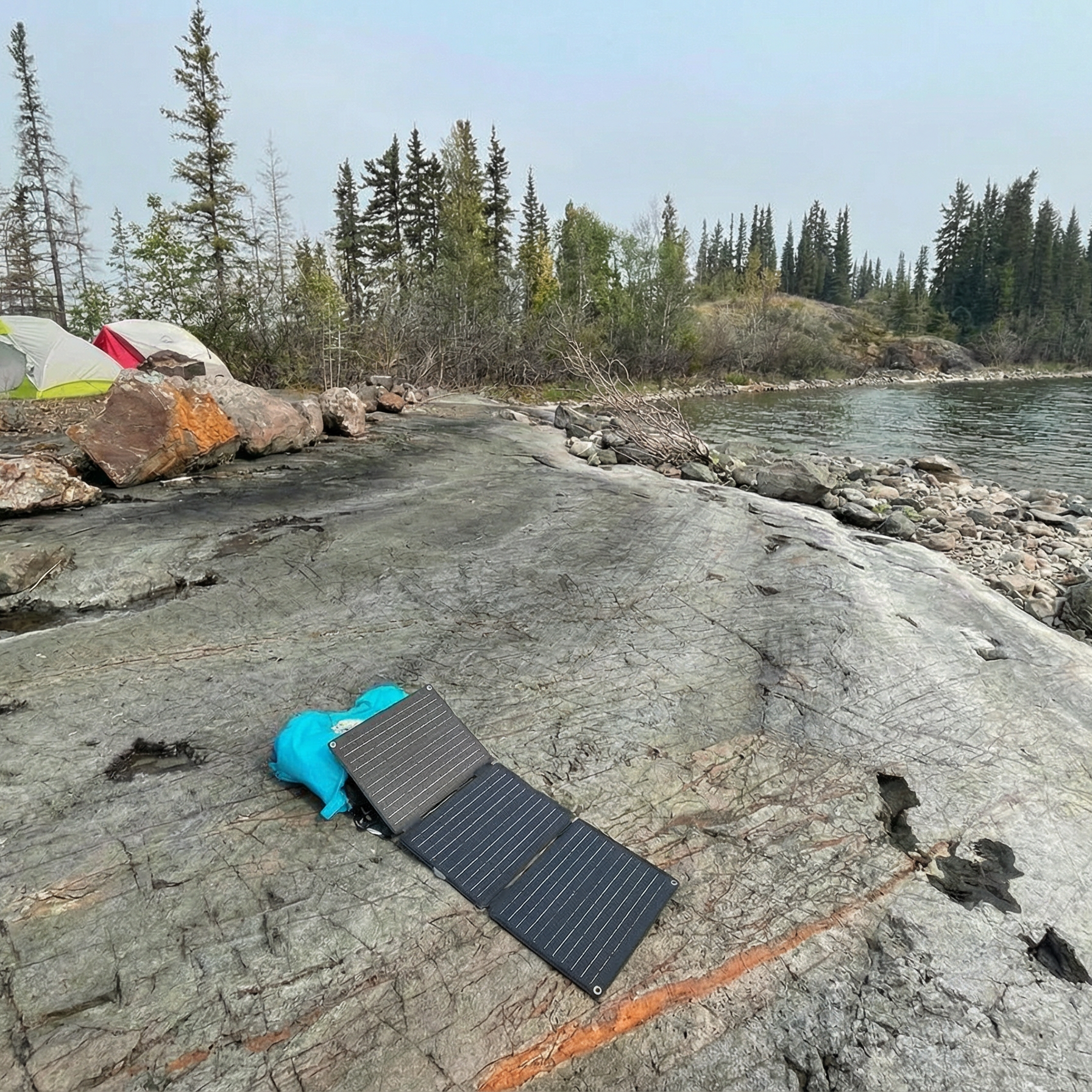 Solar panel on a rocky lakeshore with camping setup in the background