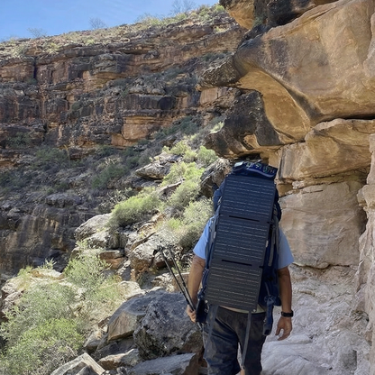 Person hiking on a rocky trail with cliffs and greenery in the background
